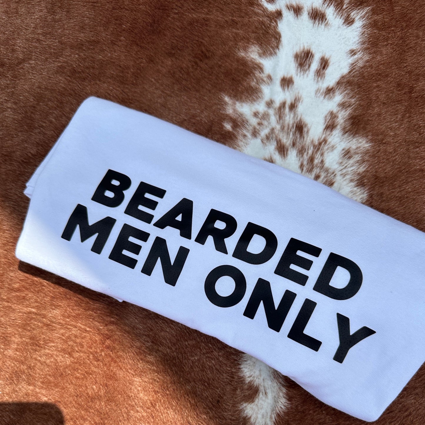 White tshirt with bold black text stating BEARDED MEN ONLY on a brown and white cow print background