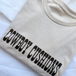 sand tshirt with brown writing cowboy cushions across the chest