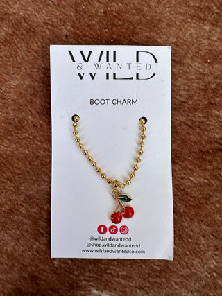Gold boot charm with red berries on a 'Wild & Swanted' card against a brown textured background