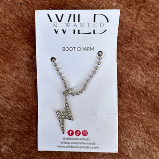 Silver boot charm on a 'Wanted & Wanted' card against a brown textured background