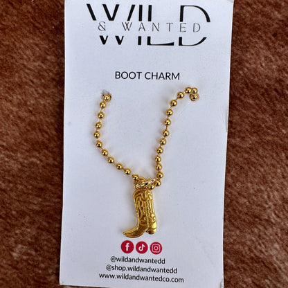 Gold boot charm on a card with 'Wild & Wanted' branding on a brown textured background